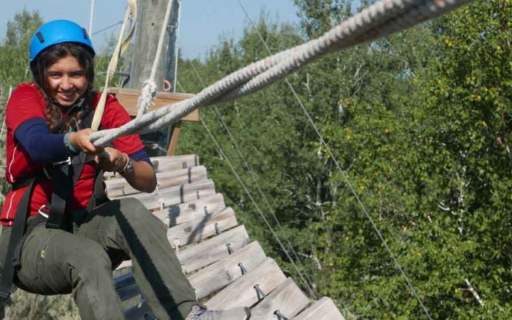 a student wearing safety gear and secured by ropes holds a rope during a ropes course with outward bound